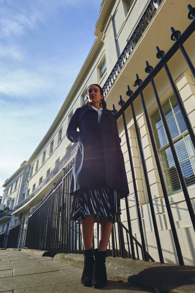 A models wears a dark AVIE trench coat on a sunny street