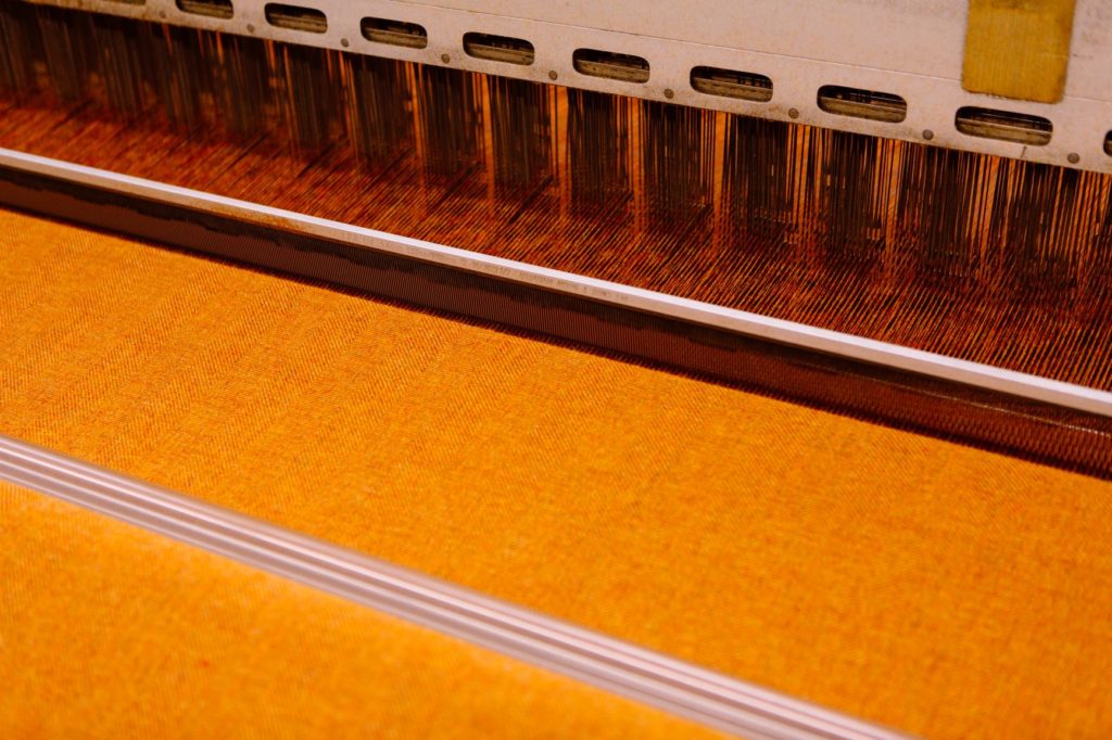 Yellow fabric being woven on a loom