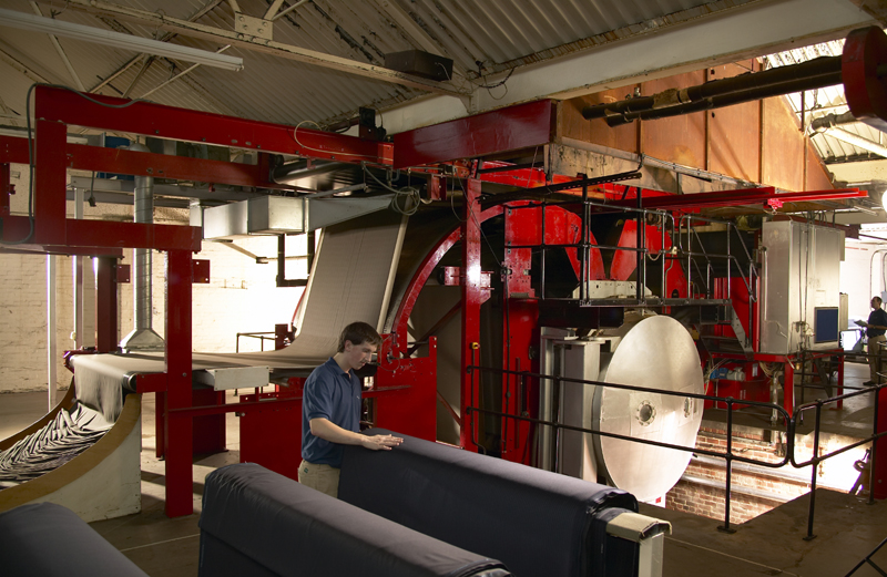 A member of staff stands inside a fabric finishing facility at WT Johnson with rolls of navy cloth being worked on