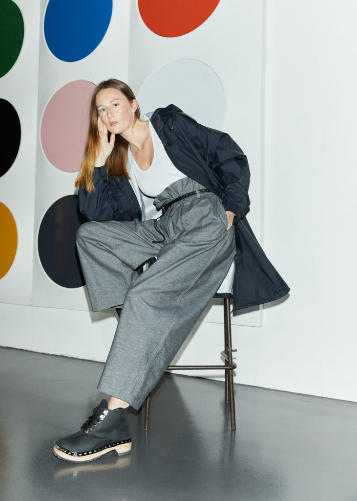 Model wears white scoop next vest wth grey gabardine trousers, navy blue mack by Nomad Atelier