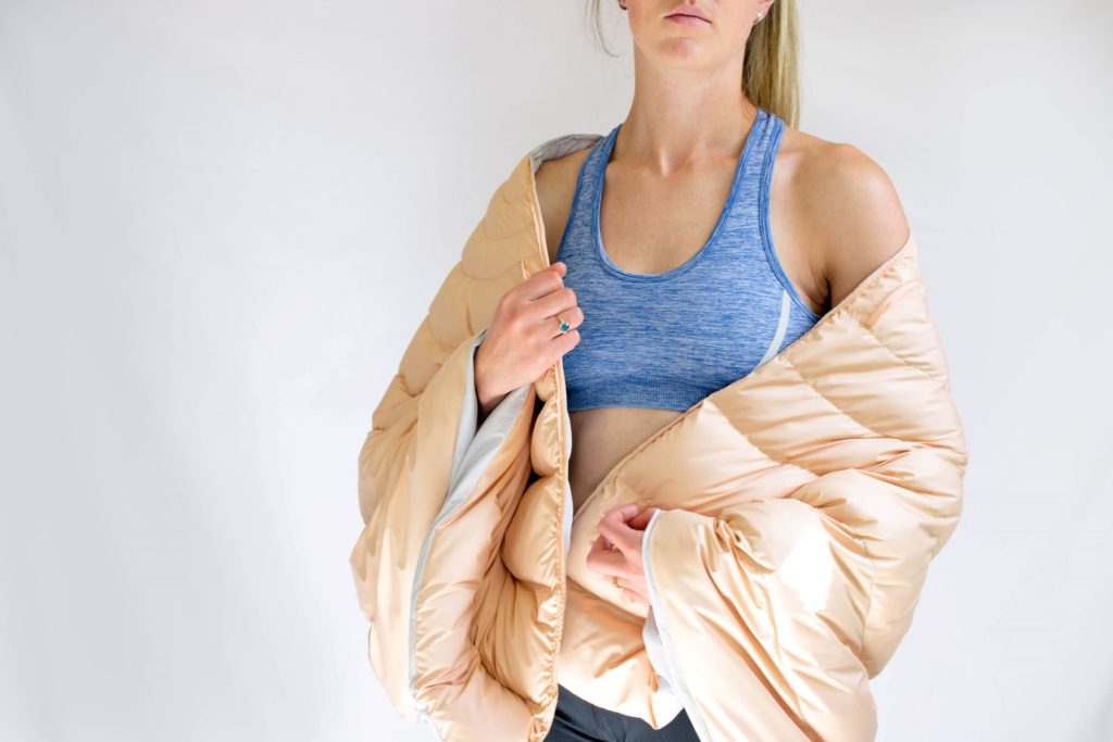 A model wears a blue crop top and a pale pink puffa-style jacket around her shoulders