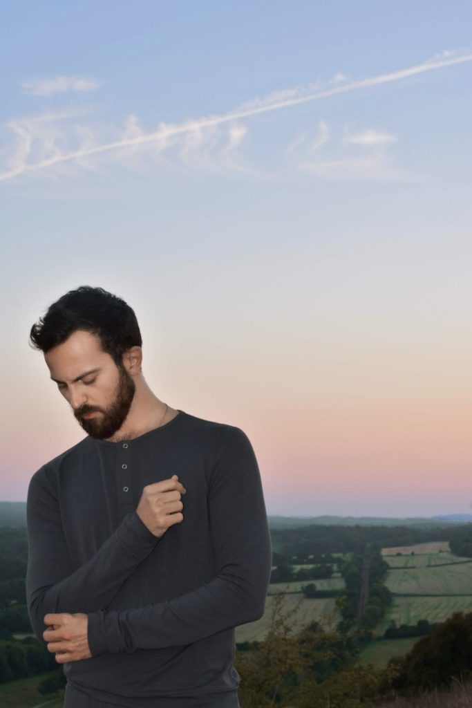 Man wearing dark grey long-sleeve top against a sunset over rolling fields