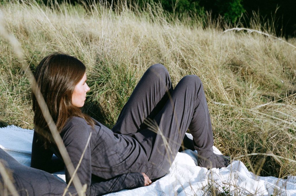 Model wears dark grey long-sleeve top, trousers and socks while lying on a blanket in a field