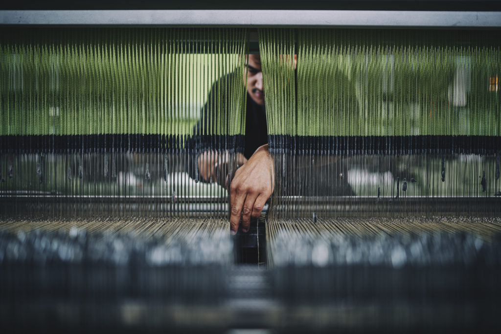 A mill worker outs his hand through the yarns on a loom