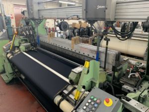 A green loom with black fabric being woven across the machine