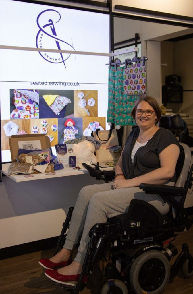 Kat Bent alongside a stand containing Seated Sewing pamper kits