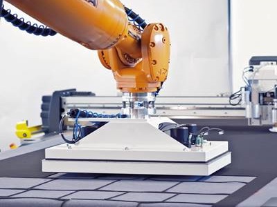 A yellow and white metal cutting machine cuts rectangles from navy fabric