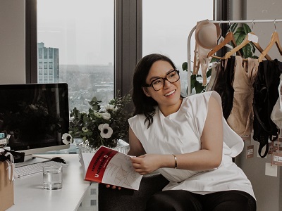 Brarista founder Bella Ngo sits against a rack of lingerie and shapewear