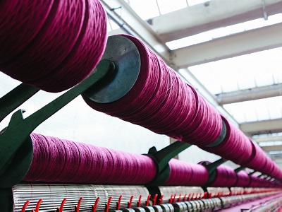 A close up of bright pink yarn on a roll connected to a loom