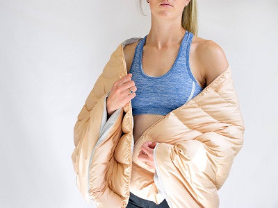 A model wears a beige-coloured insulated jacket over a blue sports crop top