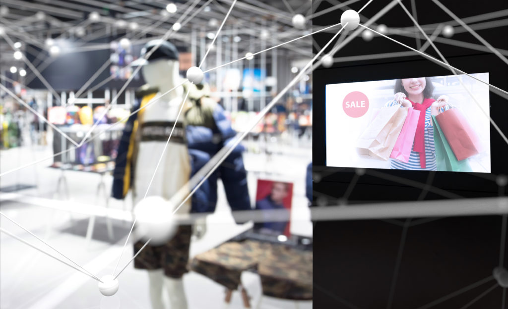 Padded jacket on a mannequin in a department store, with a screen nearby featuring a 'Sale' sign. In the foreground white lines connected by dots reach across the image.