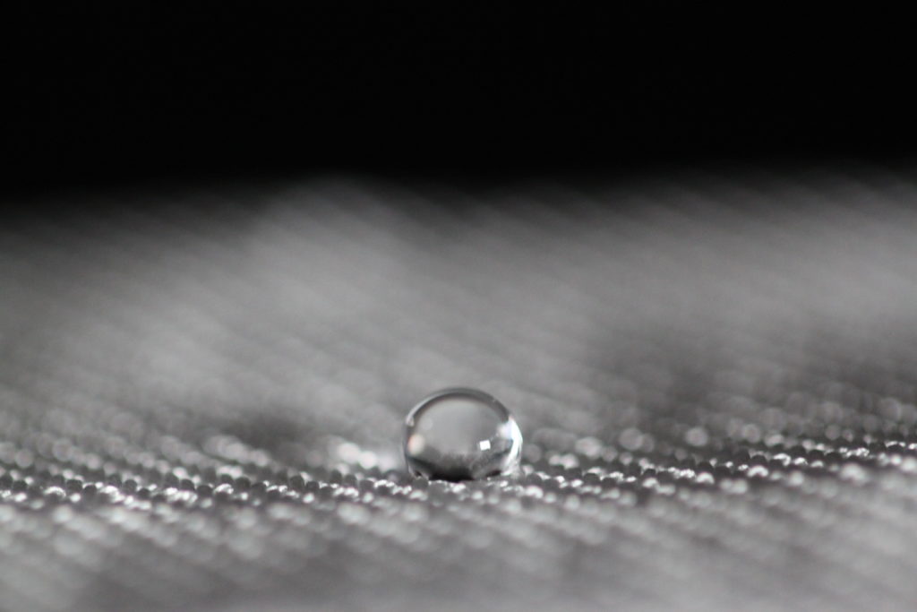 A drop of water sitting on top of a piece of grey woven fabric in close-up